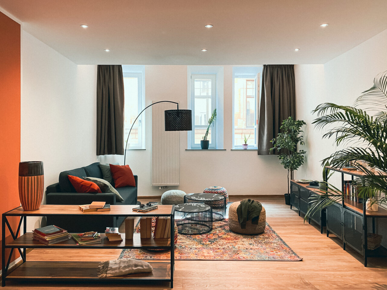 Heller Wohnraum mit dunkelgrünem Sofa, orangefarbener Wand, Palmen und hohen Fenstern