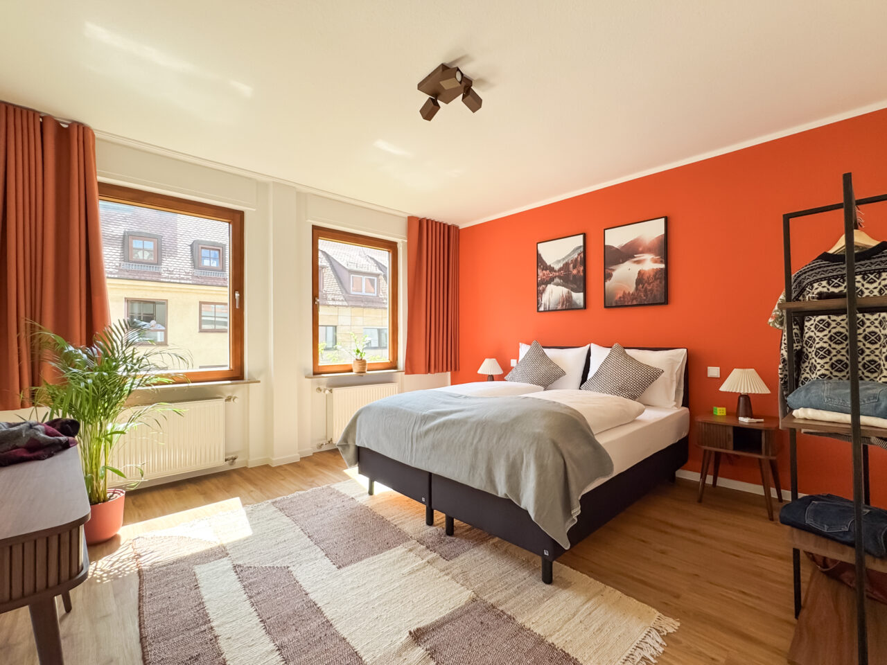 Bett vor einer orangeroten Wand mit zwei Bildern, davor ein gemusterter Teppich