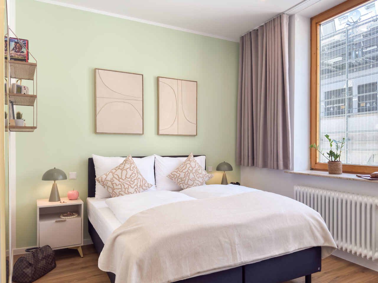 Schlafbereich mit zartgrüner Wand, hellem Bettzeug und Holzfenster